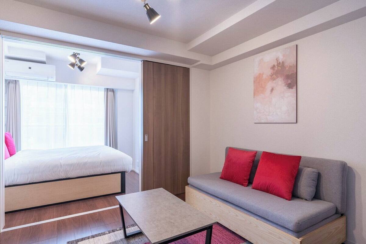 A modern hotel room with a bed, a sofa, a small table, and a painting on the wall.