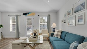 A modern living room with a teal sofa, a glass coffee table, and a dining area with a white table and chairs. - Walk to Private Beach+Free golf cart+Private Heated Pool+Pet Friendly (Destin)