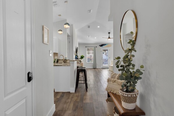 A hallway with a wooden floor, a white door, a bench with a plant, and a mirror on the wall.