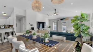 A modern living room with a glass dining table, white chairs, a teal sofa, and a large green plant. - Walk to Private Beach+Free golf cart+Private Heated Pool+Pet Friendly (Destin)