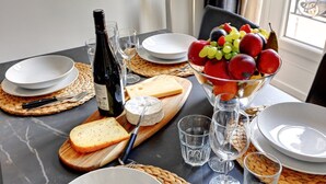 Ein gedeckter Tisch mit Tellern, Besteck, einer Weinflasche, Käse, Obst und Gläsern.