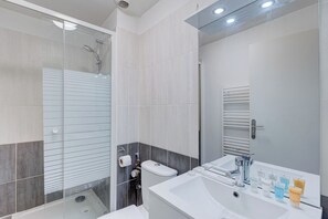 Ein modernes Badezimmer mit Duschkabine aus Glas, einem weißen Waschbecken mit Pflegeprodukten und einem Spiegel mit Handtuchhalter.