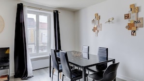 Un espace repas moderne avec une table en verre, des chaises noires et une vue sur la ville grâce à une grande fenêtre.