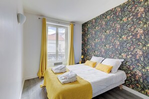 A bedroom with a bed, yellow curtains, a window, and a floral wallpaper.