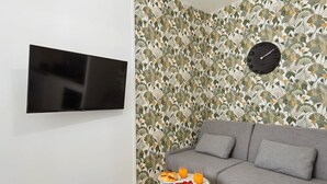 Een moderne woonkamer met een grijze bank, een flatscreen televisie aan de muur en een decoratieve wand met een klok.
