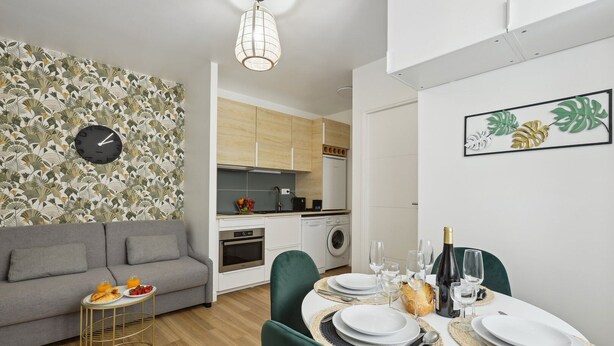 Een moderne woonkamer met een grijze bank, een eettafel voor vier personen en een keuken op de achtergrond.