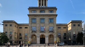 Um edifício grande e histórico com uma torre central, várias janelas e uma bandeira.