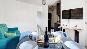 Uma sala de estar moderna com uma mesa de jantar posta para refeição, um sofá azul e uma cozinha visível ao fundo.
