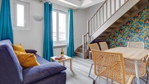 A modern living room with a sofa, table, and chairs, a staircase, and a colorful wall. - TheBlueStay 136 - Beautiful Duplex Apartment (Paris)
