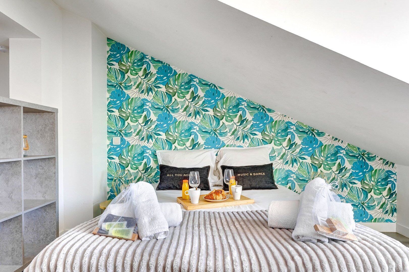 A bedroom with a large bed, a wooden side table, and a wall with a tropical leaf pattern.