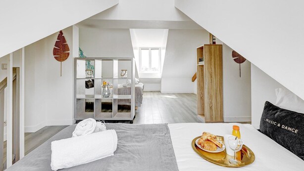 A modern, well-lit room with a loft-style ceiling, a bed with a tray of breakfast, a wooden wardrobe, and a small seating area with a table and chairs. - TheBlueStay 136 - Beautiful Duplex Apartment (Paris)