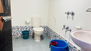 A bathroom with a toilet, bidet, sink, and a blue bucket. - Hotel Royal Palm (Sylhet)