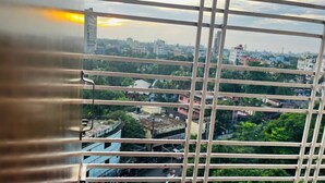 A view through a window with metal bars, featuring a cityscape with buildings and greenery. - Hotel Royal Palm (Sylhet)