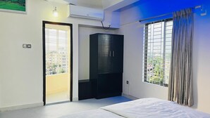 A bedroom with a bed, a wardrobe, a window with curtains, and a door leading to a balcony. - Hotel Royal Palm (Sylhet)