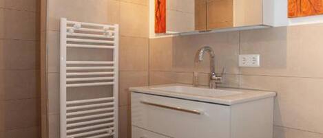 A bathroom with a white sink, a mirror above it, and a towel rack to the left.