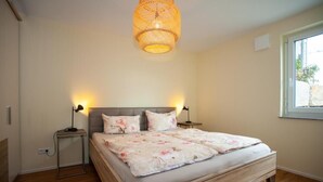 Une chambre à coucher avec un grand lit, deux lampes de chevet, un luminaire suspendu et une fenêtre donnant sur un beau paysage.