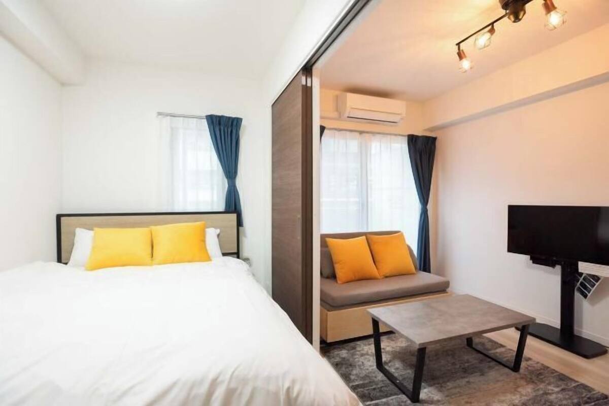A hotel room with a bed, a sofa, a coffee table, a TV, and an air conditioning unit.