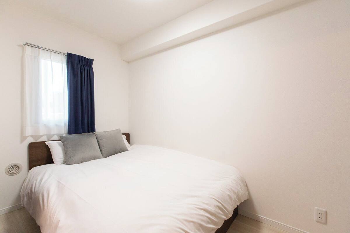 A bedroom with a bed, a window with curtains, and a wall socket.