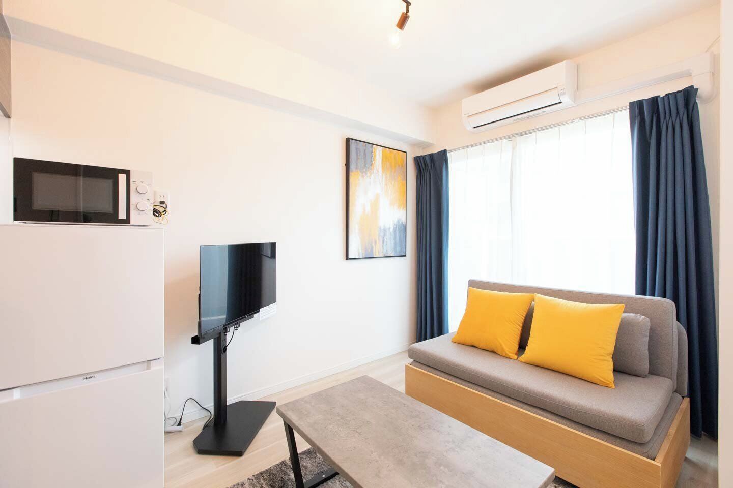 A modern living room with a flat-screen TV, a sofa with yellow cushions, a coffee table, and a microwave.