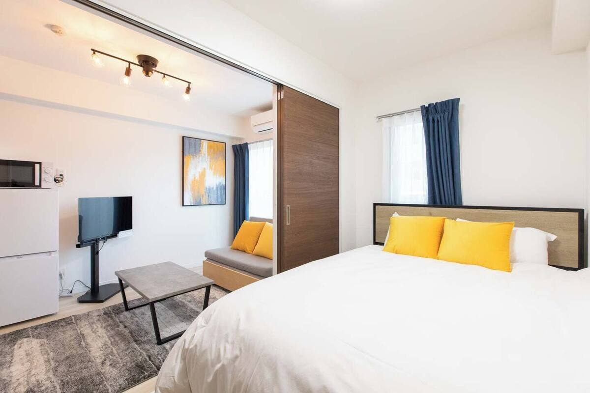 A modern hotel room with a bed, a TV, a sofa, and a desk.