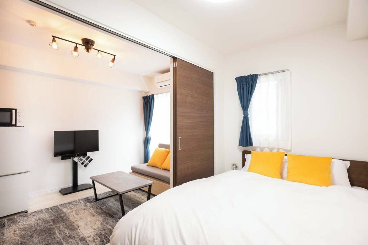 A modern hotel room with a bed, a desk, a TV, and a window with curtains.