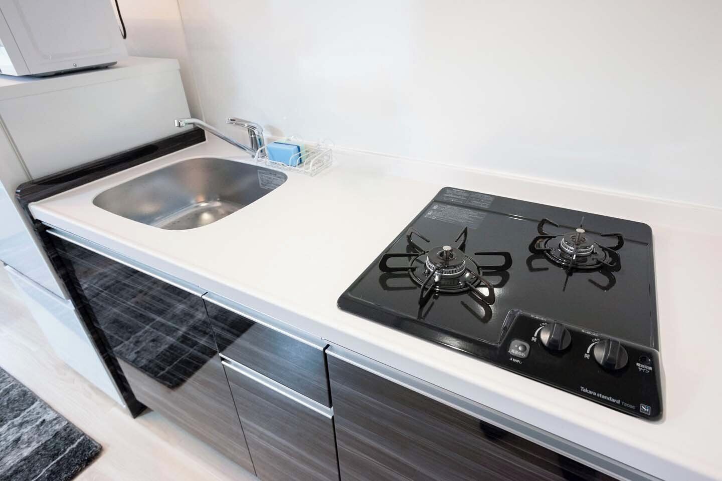 Cozinha com bancada branca, pia de aço inoxidável e fogão a gás Takara.