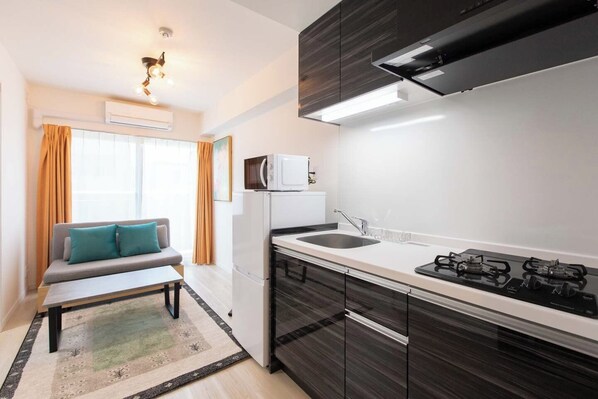 Una cocina moderna con estufa a gas, microondas y un lavaplatos. Hay un sofá con cojines y una ventana con cortinas.
