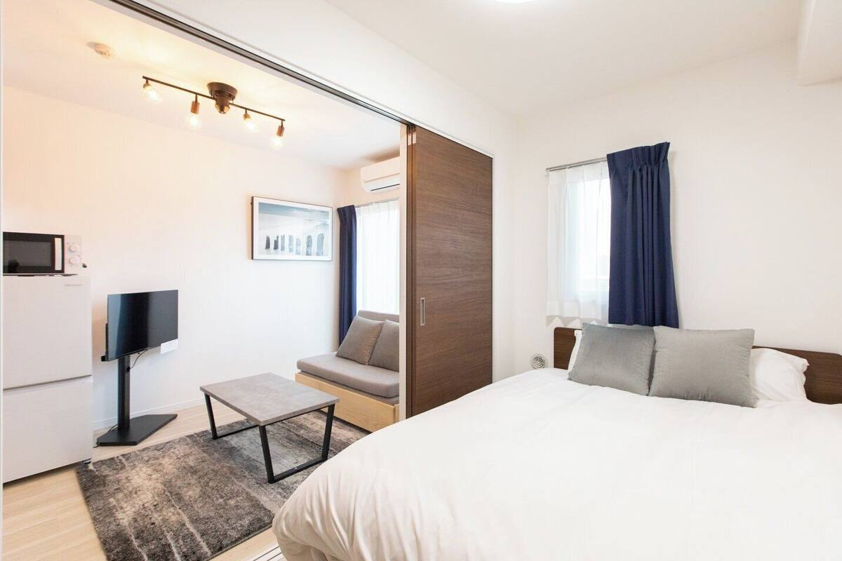 A modern hotel room with a bed, a sofa, a flat-screen TV, a microwave, and a small table.