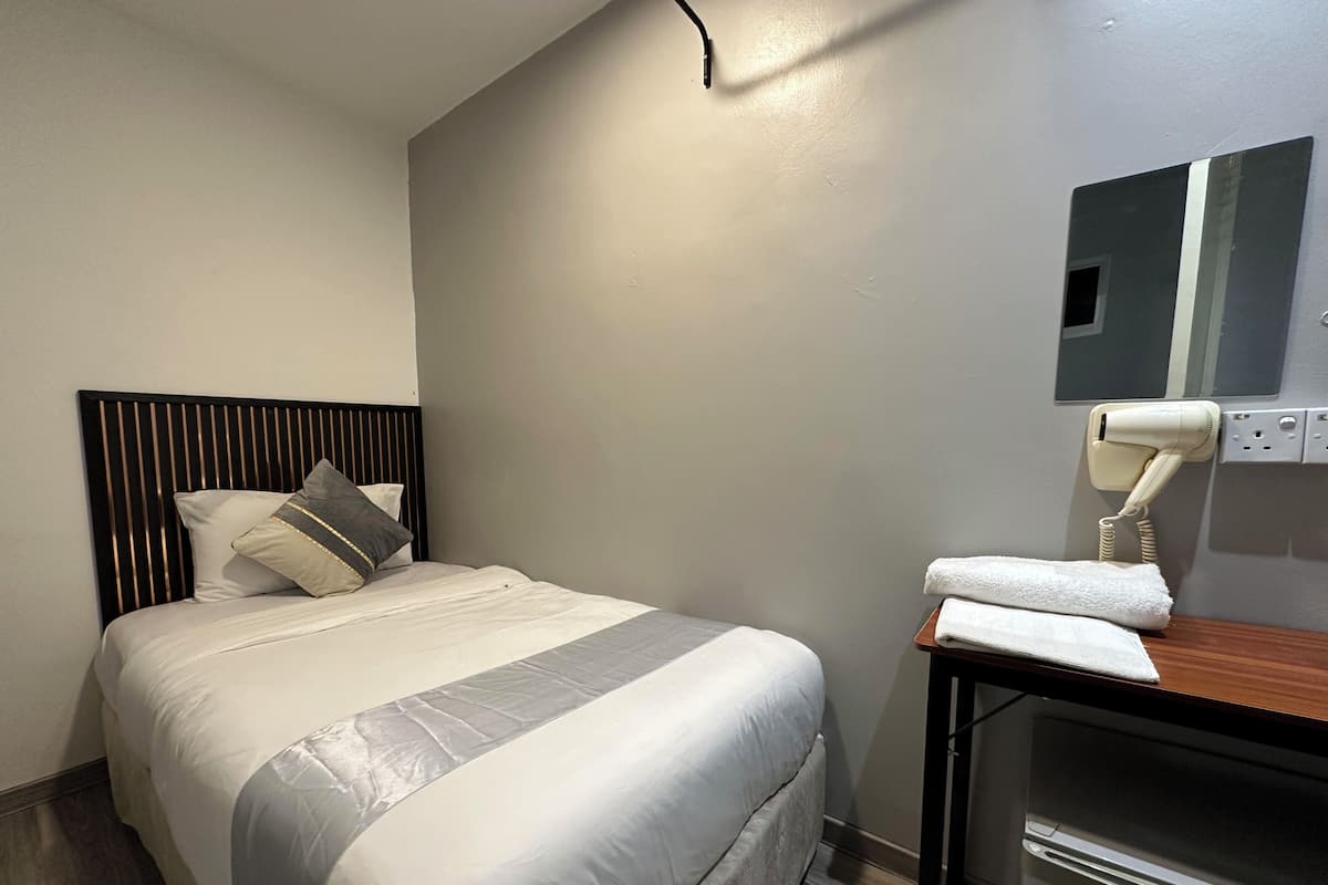 Une chambre d’hôtel avec un lit, une table de chevet équipée d’un sèche-cheveux et un miroir au mur.