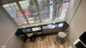 Ein Zimmerwinkel mit einem Fenster, drei Barhocker, einem weißen Stuhl und einem kleinen Tisch mit einem Laptop.
