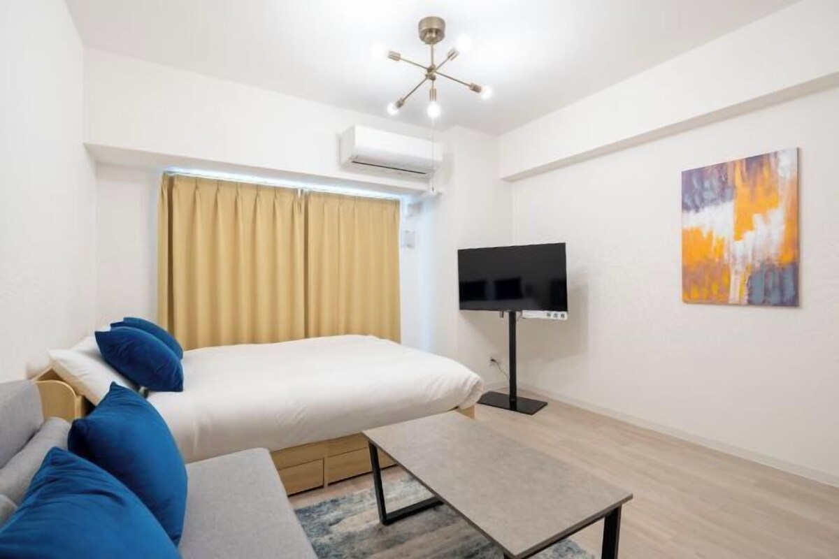 A modern hotel room with a bed, a TV, a painting, and a ceiling fan.