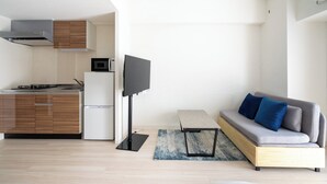Eine moderne Wohnung mit Küche, einem flachbildfernseher an der Wand, einem grauen Sofa mit blauen Kissen und einem kleinen Holztisch.