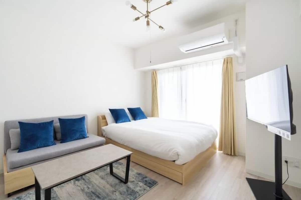 A modern hotel room with a bed, sofa, TV, and air conditioning unit.