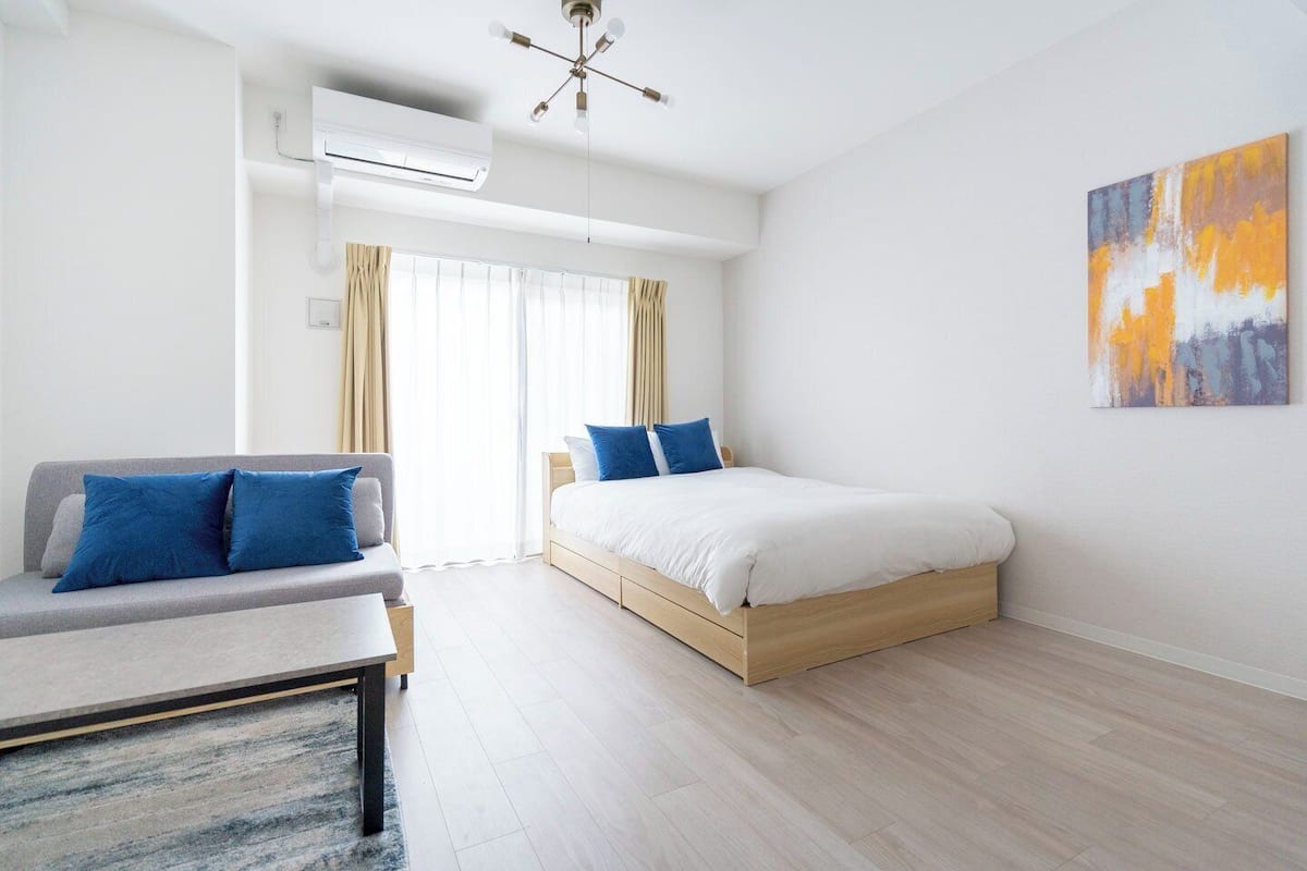 A modern hotel room with a bed, a sofa, and a large window with curtains.