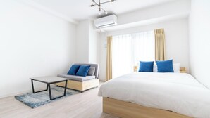 Ein modernes Hotelzimmer mit einem großen Bett, einer Couch, einem kleinen Tisch und einem Fenster mit Vorhängen.