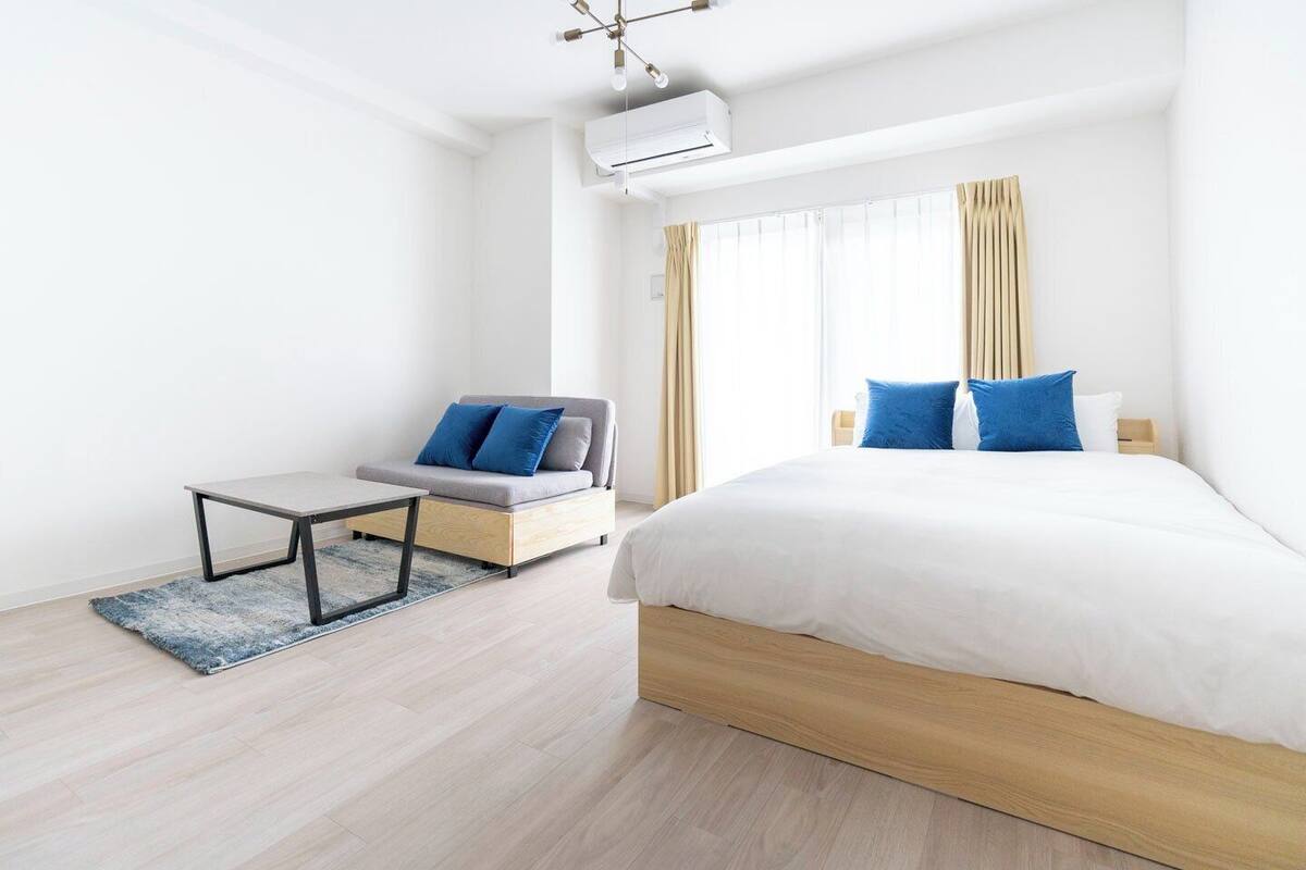 A modern hotel room with a large bed, a sofa, a small table, and a window with curtains.