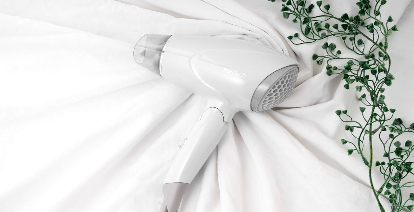 A white hair dryer on a white fabric surface with a green plant.