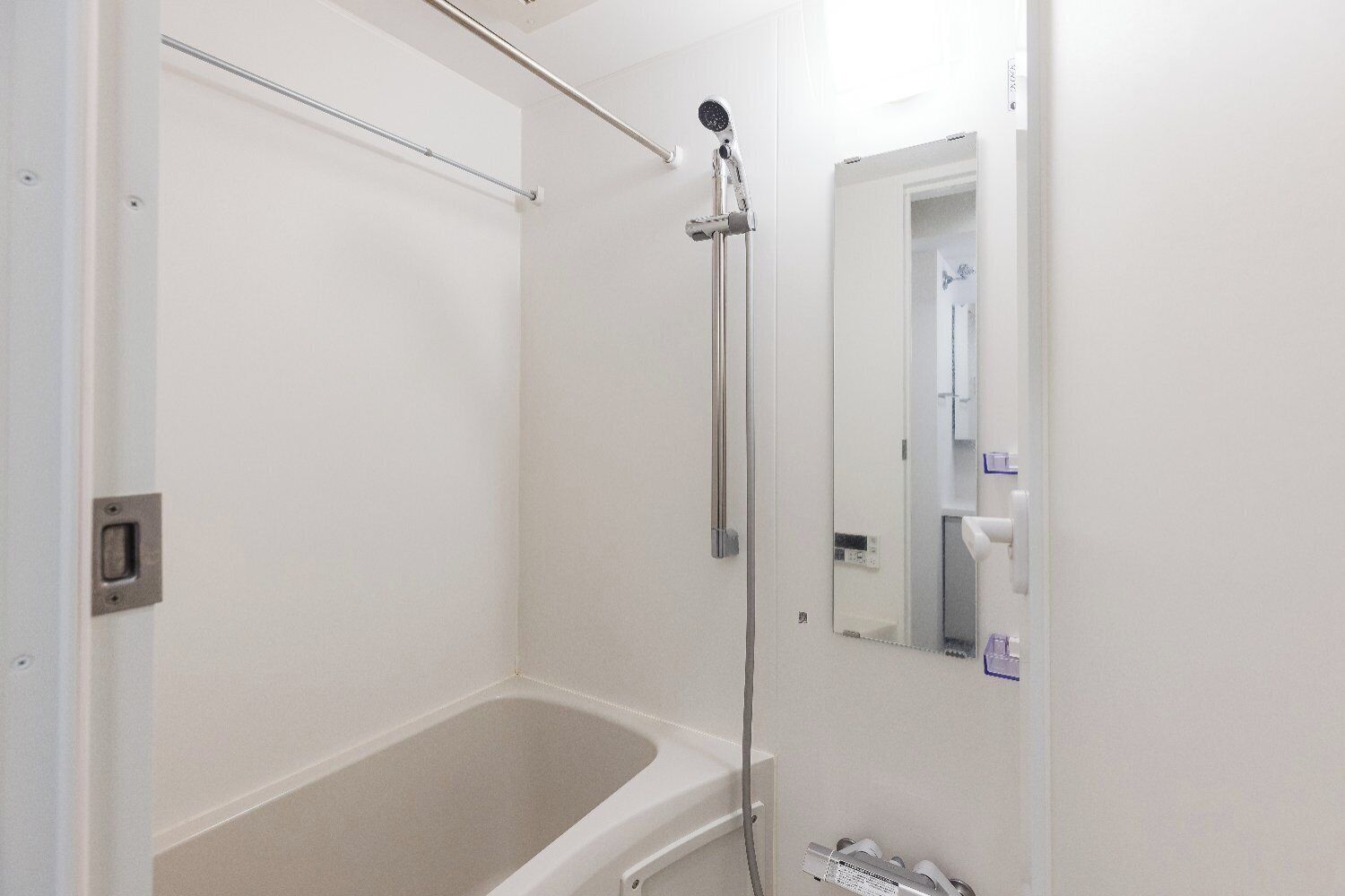 A bathroom with a bathtub, a showerhead, a towel rack, and a mirror.