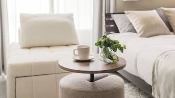 A neatly arranged bedroom with a bed, a bedside table with a cup and a plant, and a window with curtains.