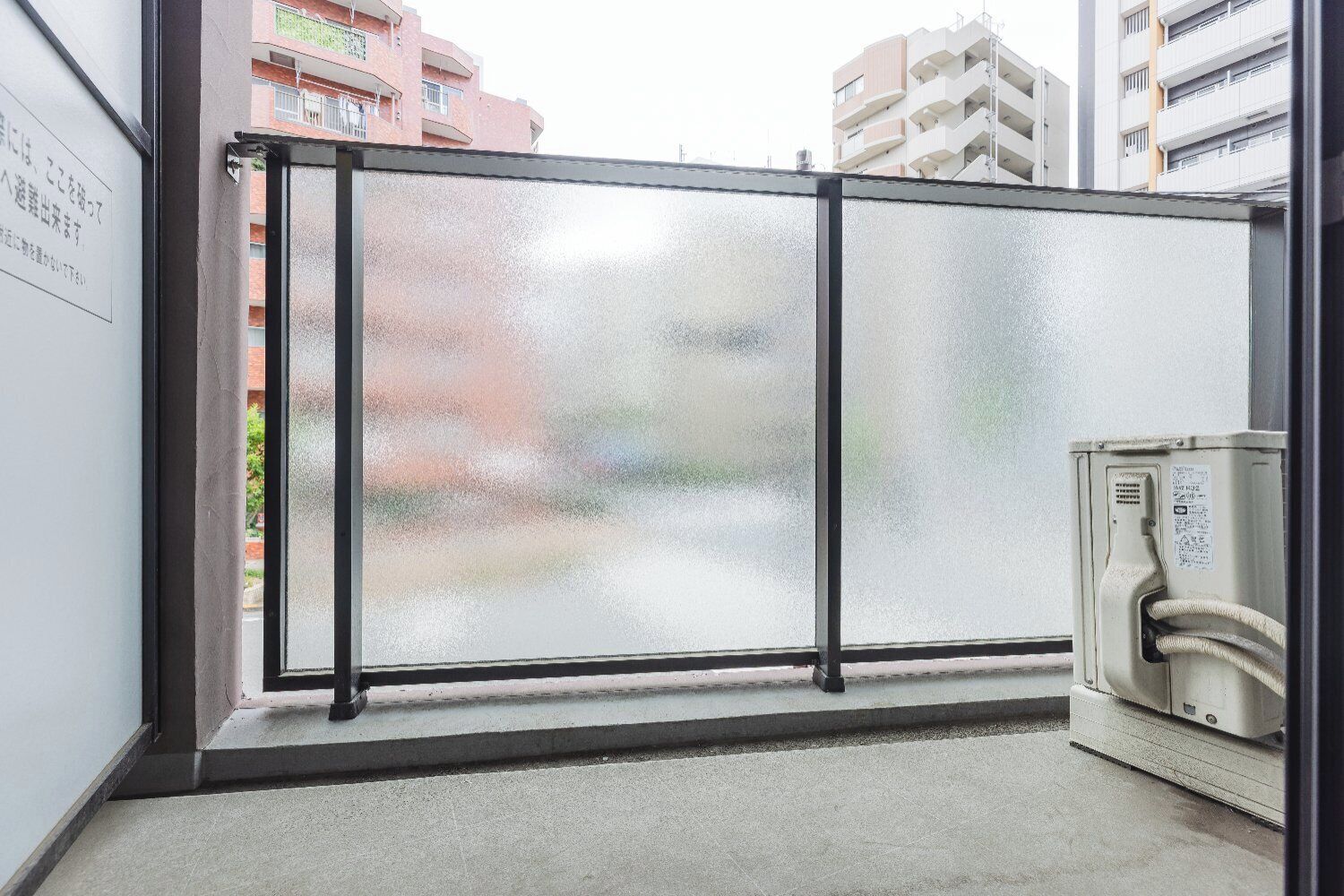 Una stanza con un divisorio in vetro, un piccolo termosifone e vista su un edificio rosso.