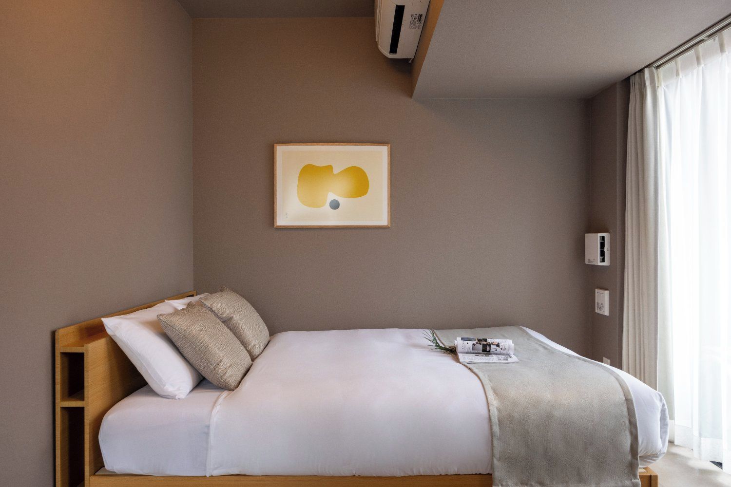 Ein Hotelzimmer mit einem Bett, Kissen, einer Decke, einer Wand-Klimaanlage und einem Fenster mit Vorhängen.