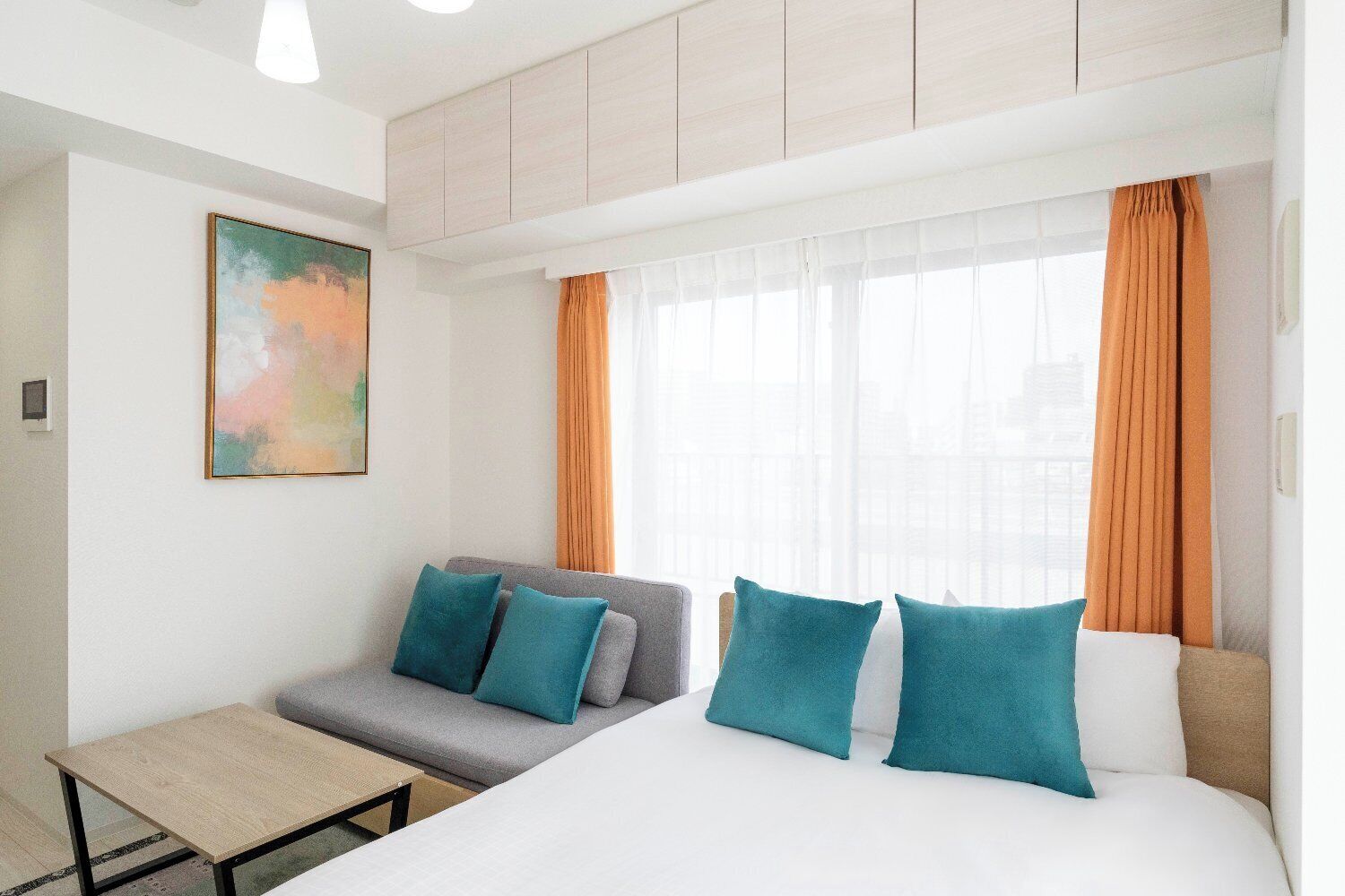 A hotel room with a bed, a sofa, a small table, and a painting on the wall.