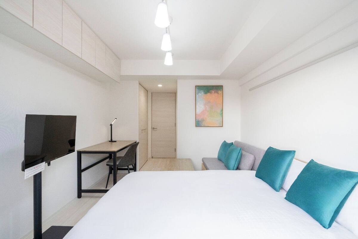 Ein modernes Hotelzimmer mit einem großen Bett, einem Schreibtisch mit Stuhl, einem Fernseher und einem Bild an der Wand.