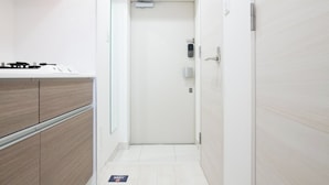 A narrow hallway with a white door at the end, a small air conditioning unit above it, and a light switch on the wall. - Prere Duque Omorimachi II (Tokyo)
