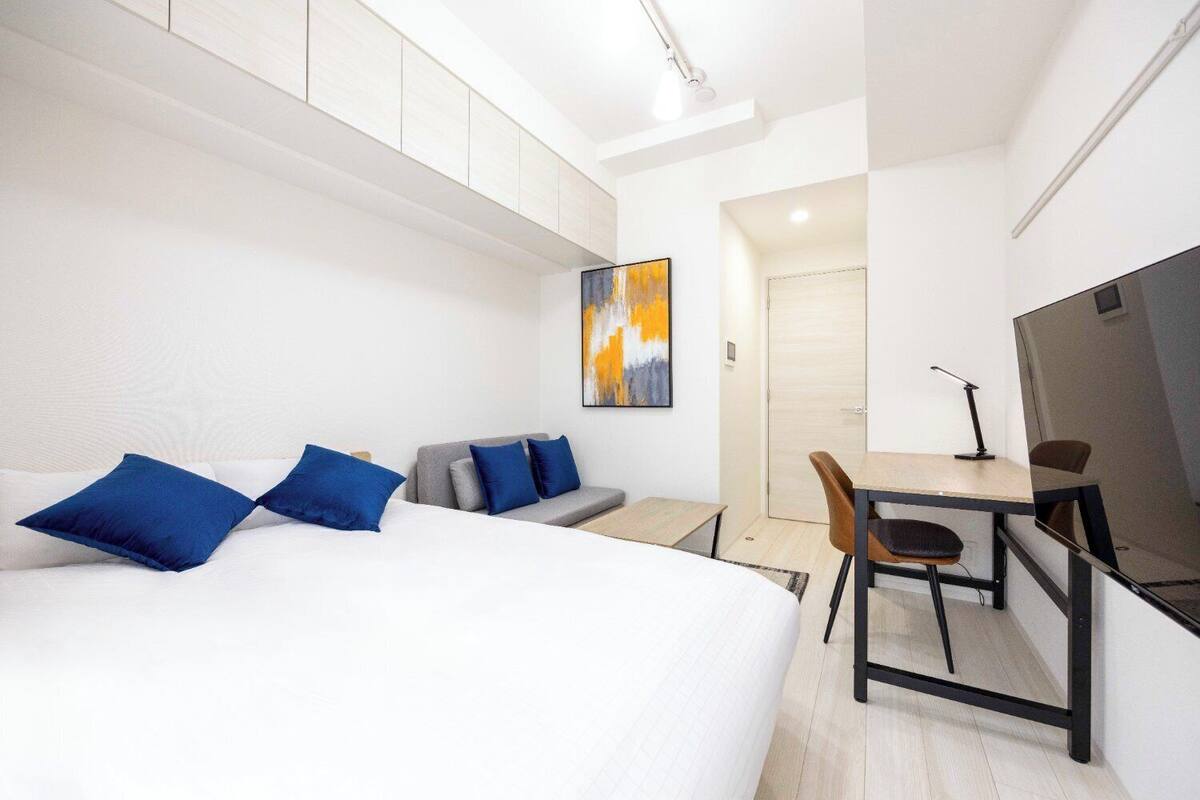 A modern hotel room with a large bed, a desk, and a sofa.