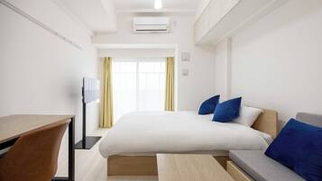 A hotel room with a bed, a desk, a chair, a sofa, and a window with curtains.