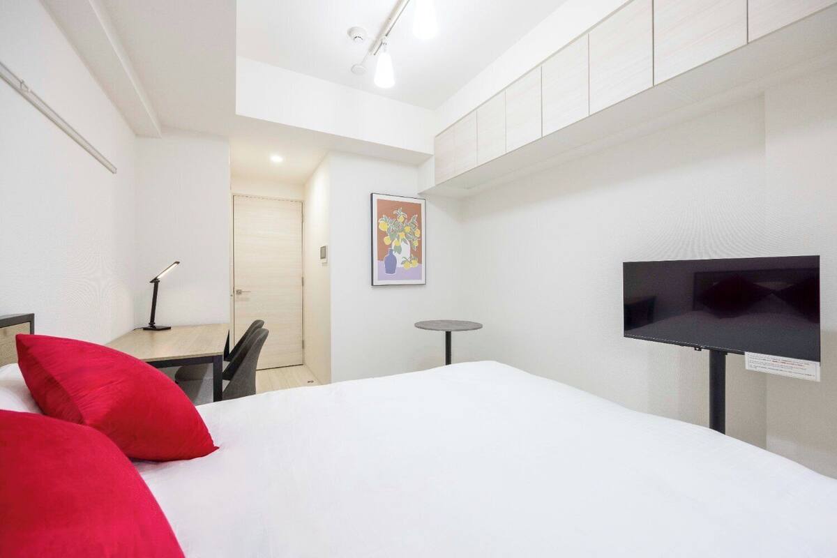 Ein Hotelzimmer mit einem Bett, einem Schreibtisch mit Stuhl, einem kleinen Tisch, einem Fernseher und einer Tür zu einem anderen Raum.