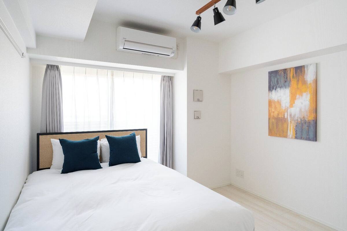 Ein modernes Hotelzimmer mit einem großen Bett, weißer Bettwäsche, einer Deckenklimaanlage und einem Gemälde an der Wand.