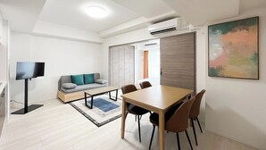 A modern hotel room with a dining area, a sofa, a TV, and an air conditioning unit. - Prere Duque Omorimachi II (Tokyo)
