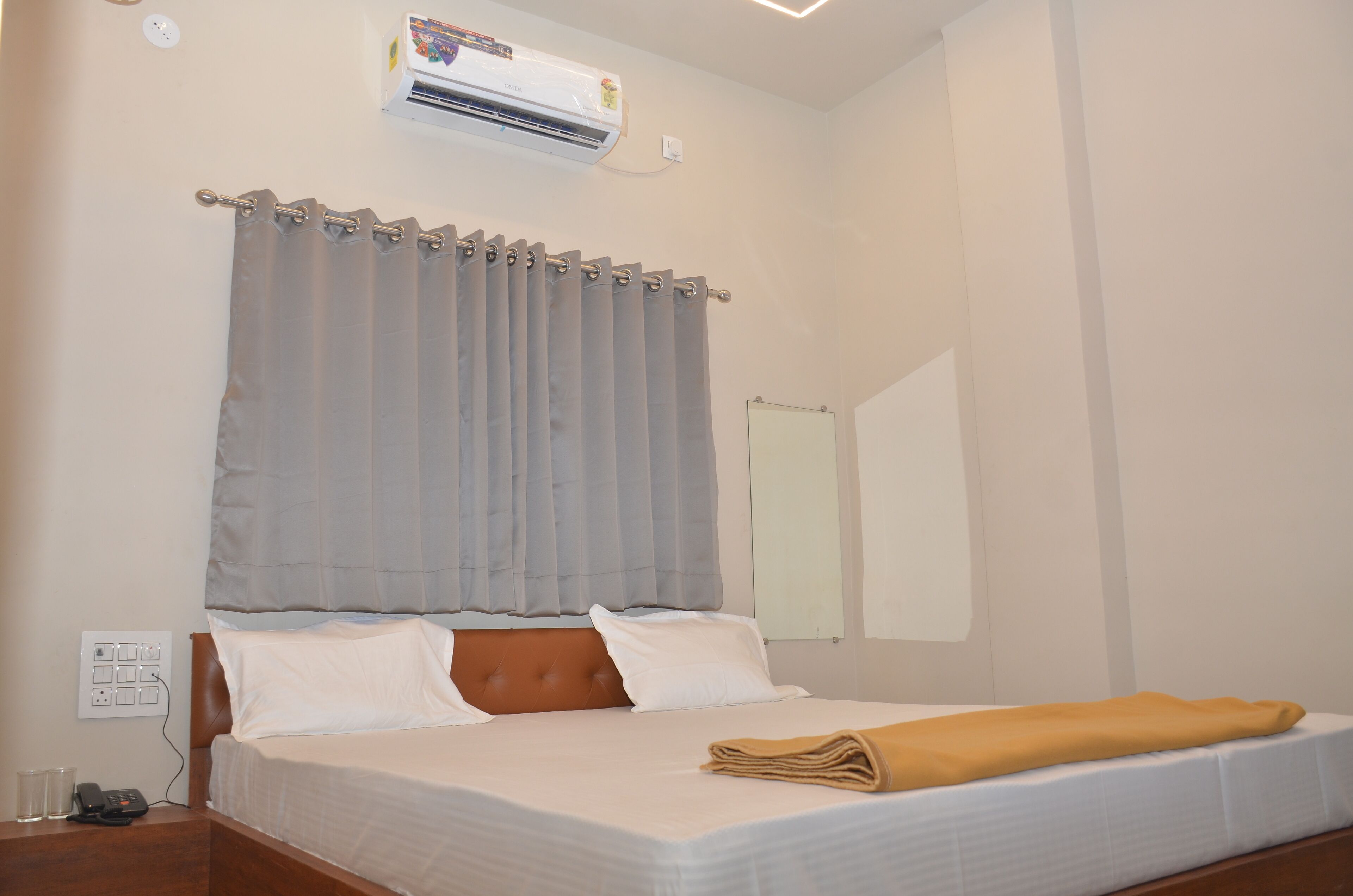 A hotel room with a bed, a bedside table, an air conditioning unit, and a curtain.